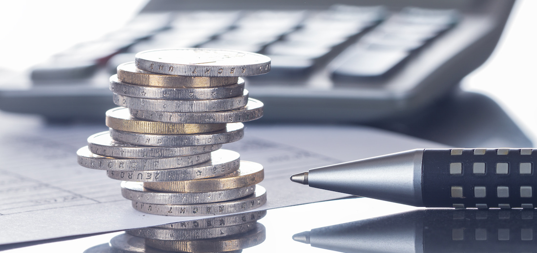 Ein Schreibtisch mit einer Tastatur im Hintergrund, im Vordergrund ein Stapel Münzen.
